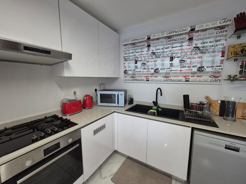 Modern kitchen featuring gloss white cabinetry, stone countertops, integrated dishwasher, gas cooktop, and a sleek black undermount sink with gooseneck faucet.