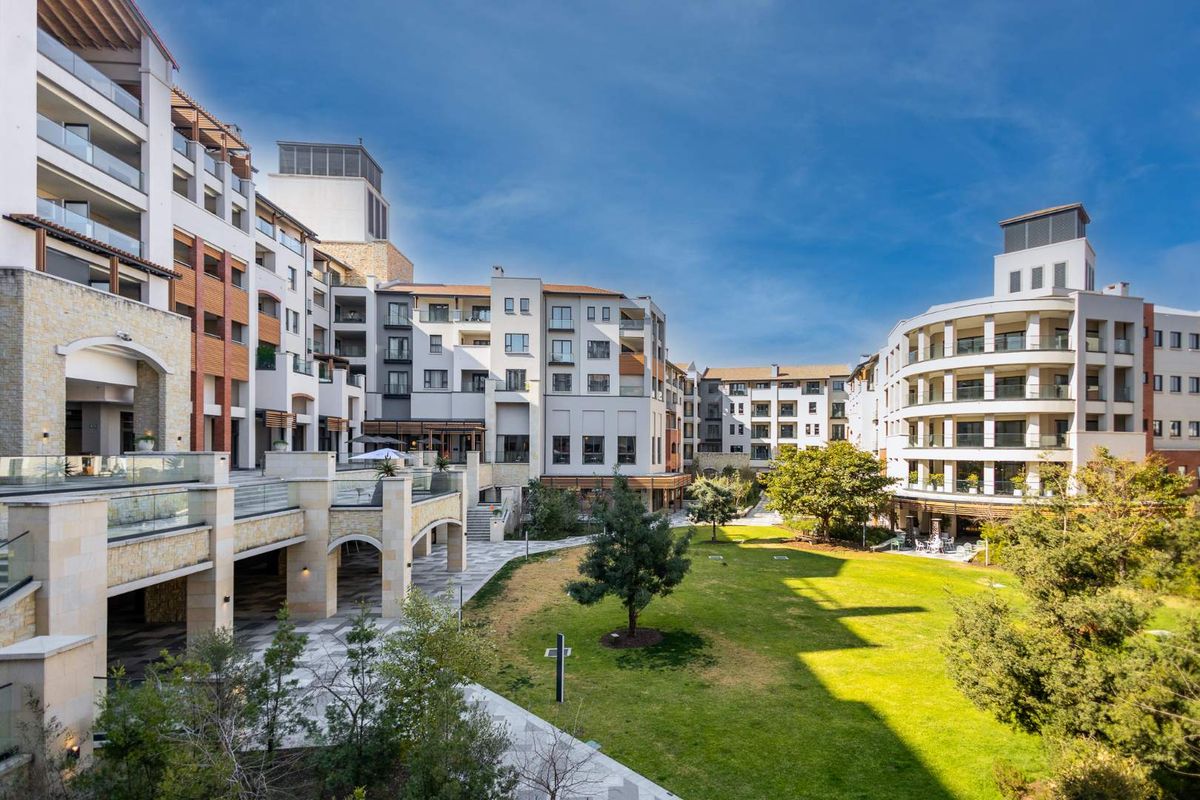 A wide-angle view of the apartment complex courtyard, featuring landscaped gardens, paved walkways, and modern multi-story residential building facades.