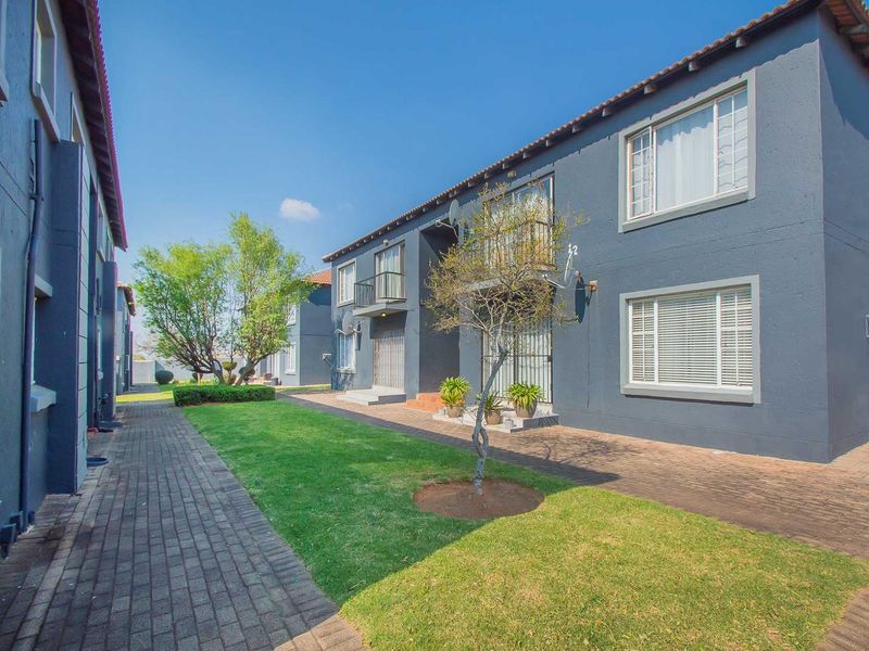 A view of the rear exterior of the apartment complex, featuring a paved walkway, manicured lawn, and balconies.