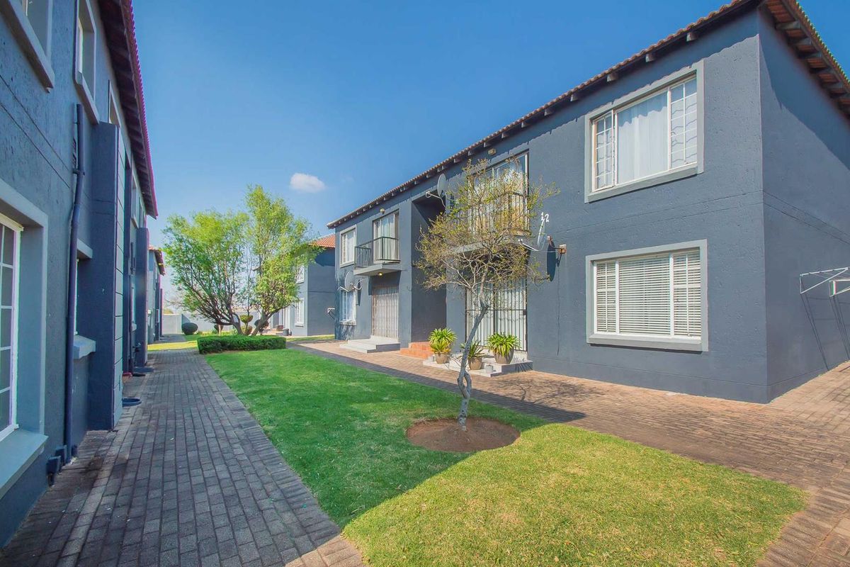 A view of the rear exterior of the apartment complex, featuring a paved walkway, manicured lawn, and balconies.