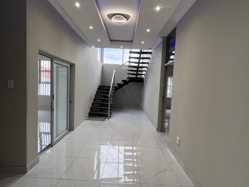 Modern hallway featuring polished marble-look floor tiles, a striking floating staircase with stainless steel railings, and sophisticated recessed ceiling lighting.