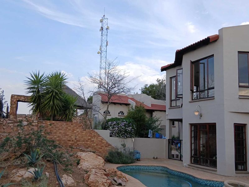 Rear exterior view featuring a swimming pool, stone retaining wall, and multi-story residential building with tiled roofing and large windows.