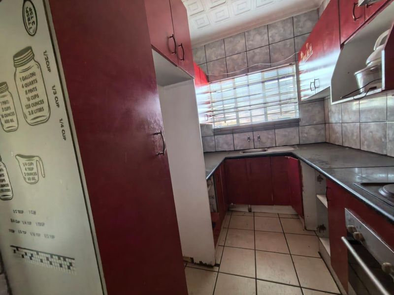 A dated kitchen featuring red cabinetry, tiled backsplash, and built-in oven, requiring cosmetic updates to modernize the space.
