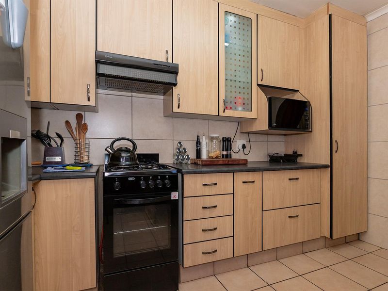 A functional kitchen featuring light wood-look cabinetry, dark countertops, a freestanding oven with extractor fan, and tiled flooring throughout.