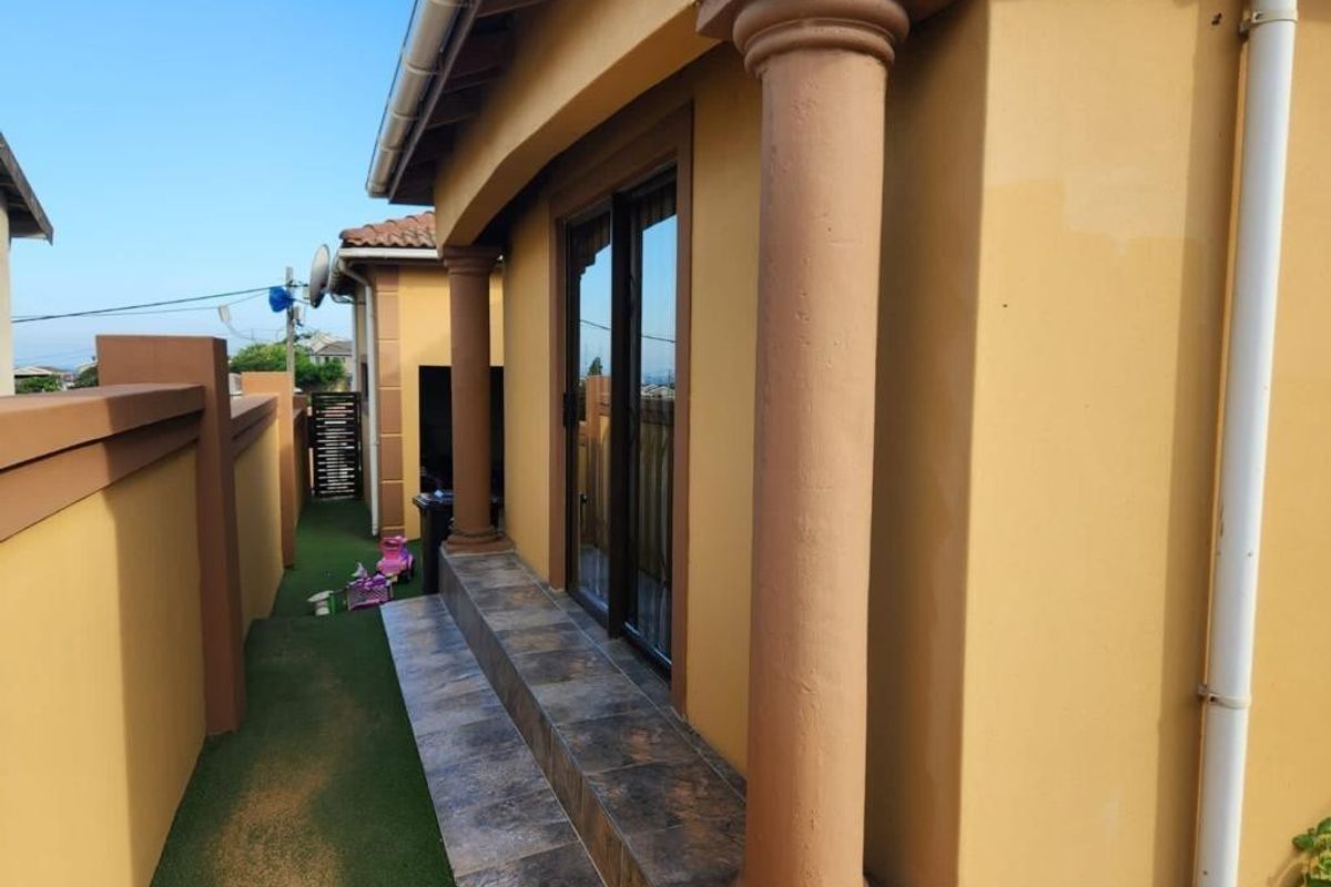 A side exterior view featuring a tiled patio area with decorative columns and sliding glass door access to the home.