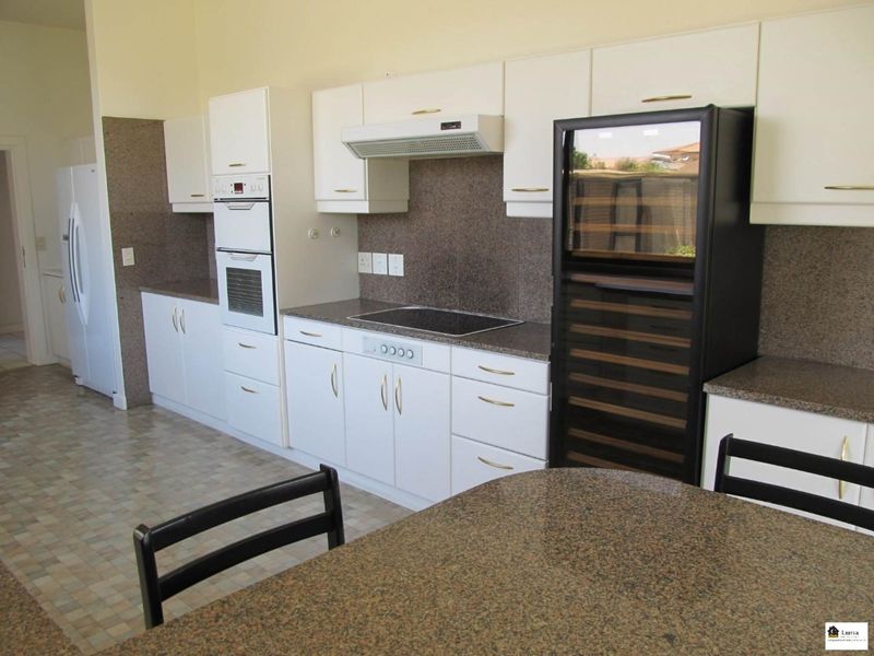 A functional kitchen featuring white cabinetry, granite countertops, a built-in oven, electric hob, extractor fan, and a dedicated wine cooler.