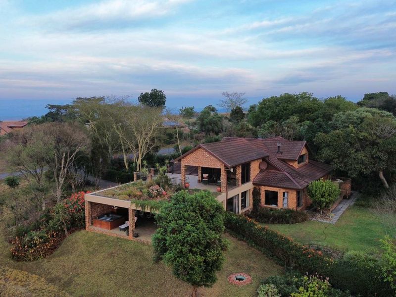 Aerial view of a multi-level brick residence featuring a tiled roof, covered patio, and an expansive landscaped garden setting.