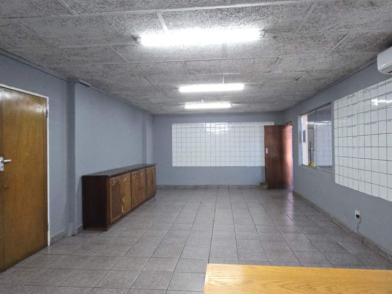 Spacious industrial office area featuring tiled flooring, acoustic ceiling tiles, wall-mounted air conditioning, and built-in storage cabinetry.