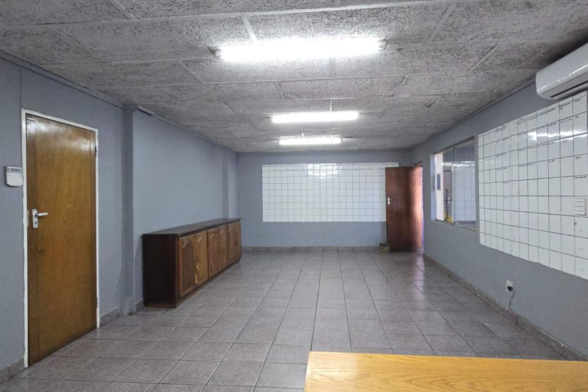 Spacious industrial office area featuring tiled flooring, acoustic ceiling tiles, wall-mounted air conditioning, and built-in storage cabinetry.