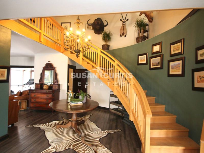 Spacious entrance hall featuring a prominent curved wooden staircase with a mezzanine landing and dark laminate flooring.