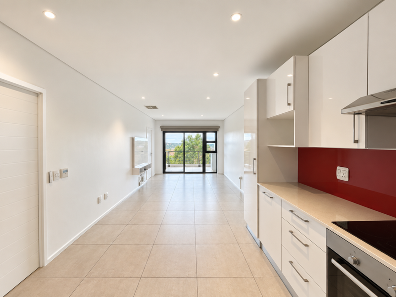 Modern open-plan living area featuring a sleek kitchen with stone countertops, integrated appliances, and large sliding doors leading to a balcony.