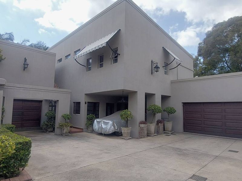 Front elevation of a modern townhouse featuring a double garage, paved driveway, and neutral plastered exterior walls with retractable window awnings.