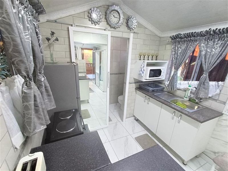 Compact kitchen featuring white cabinetry, stainless steel sink, tiled splashbacks, and tiled flooring, with direct access to an adjacent bathroom area.