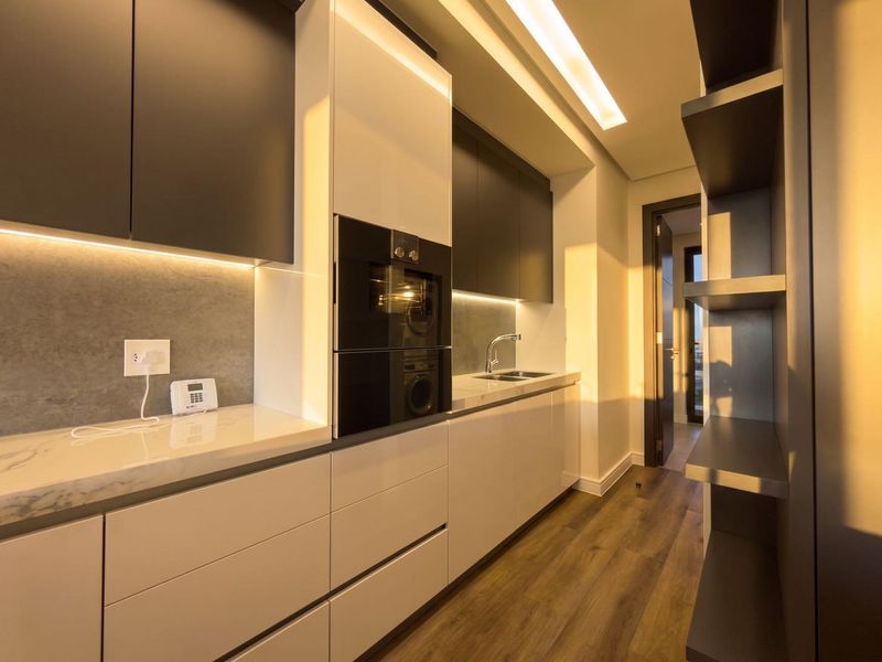 Modern, high-end kitchen featuring sleek handleless cabinetry, integrated oven, stone countertops, and warm under-cabinet lighting with high-quality finishes throughout.
