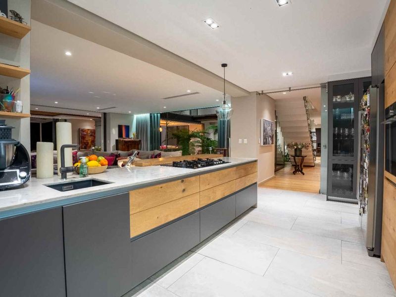 Modern open-plan kitchen featuring a large island with stone countertops, gas cooktop, and integrated cabinetry, flowing seamlessly into the living area and staircase.