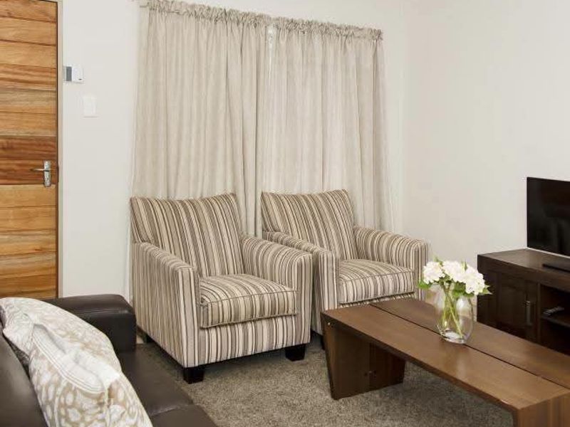 A comfortable living room featuring neutral carpet flooring, a solid timber door, and window curtain tracks.