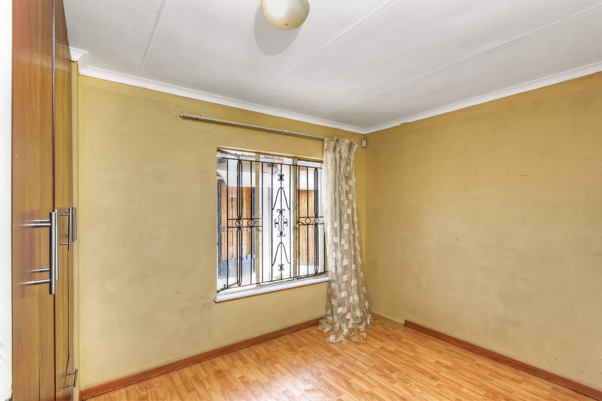 A bedroom featuring built-in wooden cupboards, laminate flooring, and a window fitted with security bars.