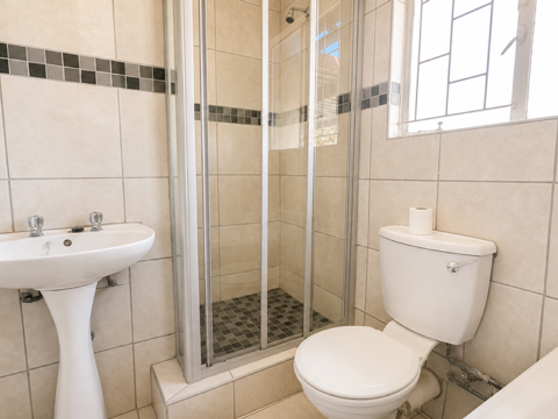 A functional bathroom featuring a pedestal washbasin, a shower enclosure with glass doors, and a standard toilet, finished with neutral wall tiling.