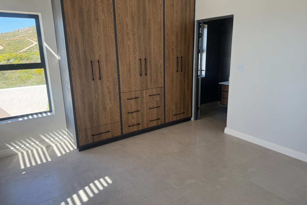 A modern bedroom featuring built-in wood-grain cabinetry, tiled flooring, and an en-suite bathroom entrance with scenic hillside views.