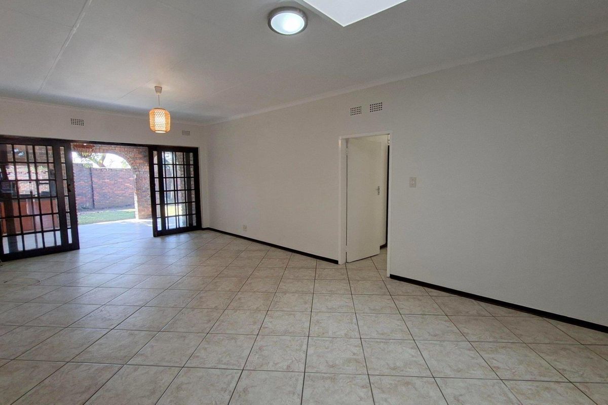 Spacious, empty living area featuring neutral tiled flooring, a skylight, and large sliding glass doors providing direct access to the outdoor patio area.