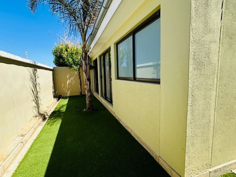 A side garden area featuring artificial turf, boundary walls, and modern aluminium window frames along the exterior wall of the townhouse.