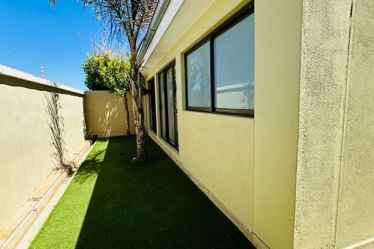 A side garden area featuring artificial turf, boundary walls, and modern aluminium window frames along the exterior wall of the townhouse.