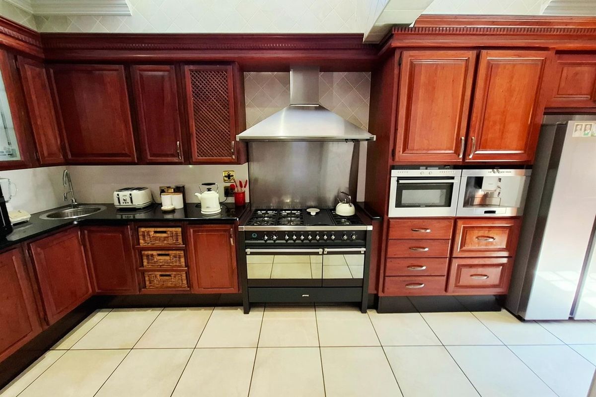 A traditional kitchen featuring dark wood cabinetry, black granite countertops, a stainless steel extractor fan, and a built-in oven with a gas range.
