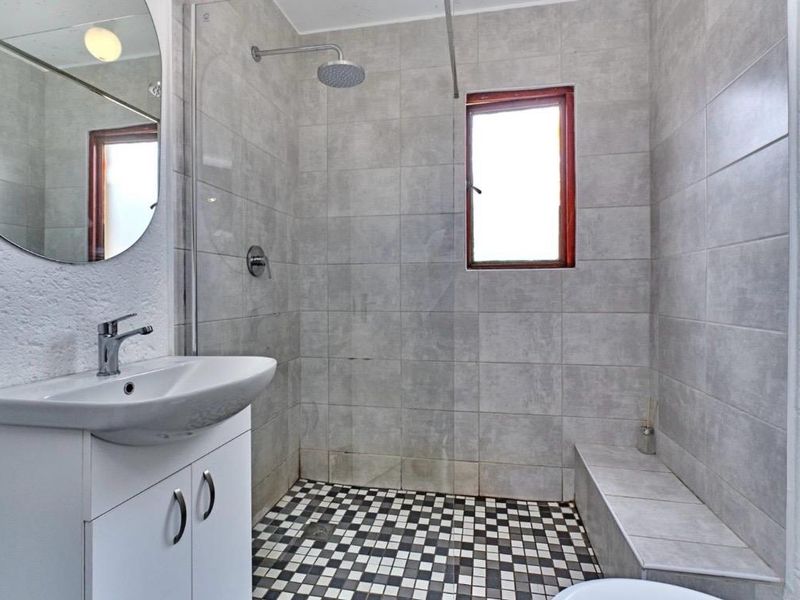 A functional bathroom featuring a walk-in shower with a built-in tiled bench, modern vanity cabinet, and neutral wall tiling.