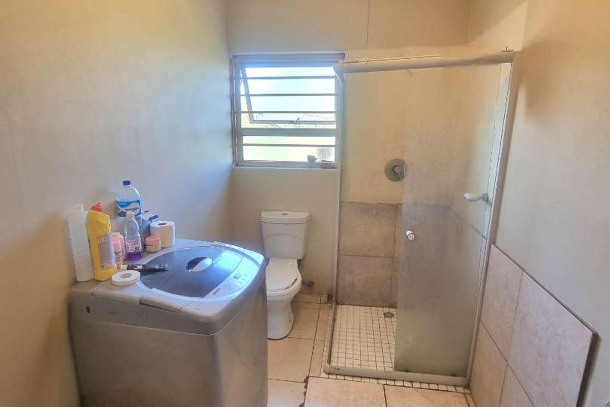 A functional bathroom featuring a tiled shower enclosure, toilet, and dedicated space for laundry appliances with tiled flooring throughout.