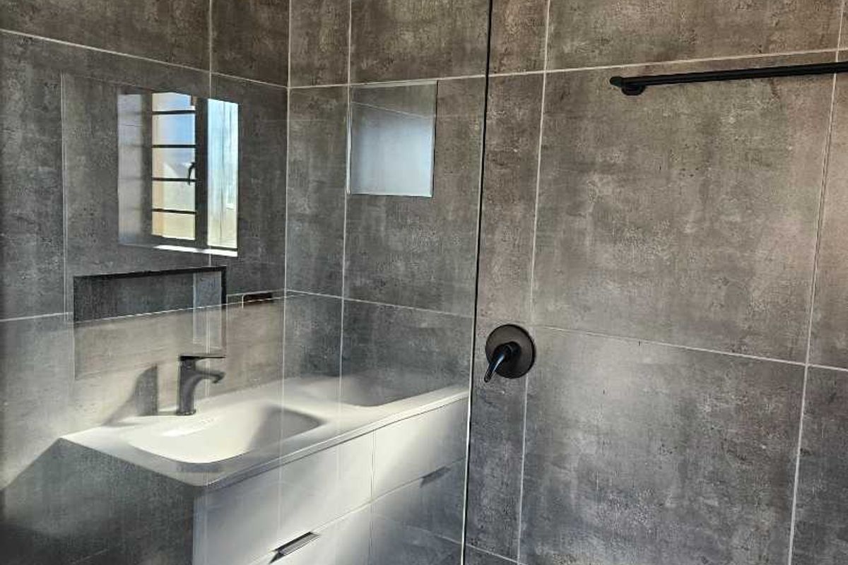 Modern bathroom featuring large format grey tiles, a wall-mounted vanity with integrated basin, and a walk-in shower with matte black fixtures.