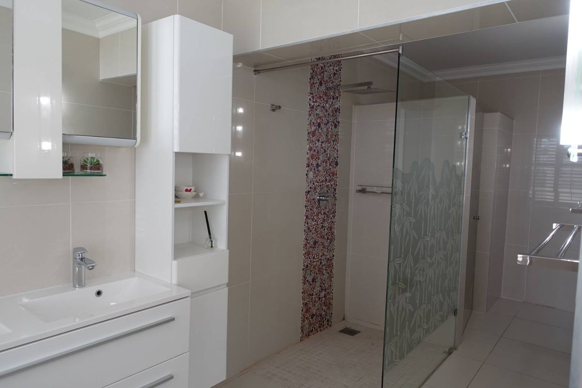Modern bathroom featuring a walk-in glass shower with mosaic tile accent, a sleek vanity with integrated basin, and wall-mounted storage cabinetry.
