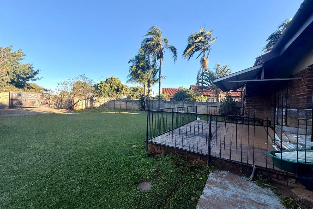 Spacious rear garden featuring a paved patio area with metal railings, established lawn, and perimeter boundary walling.