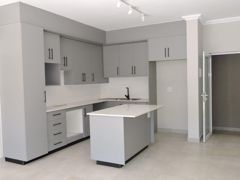 Modern kitchen featuring grey cabinetry, white stone countertops, a central island, subway tile backsplash, and sleek black fixtures in an open-plan layout.