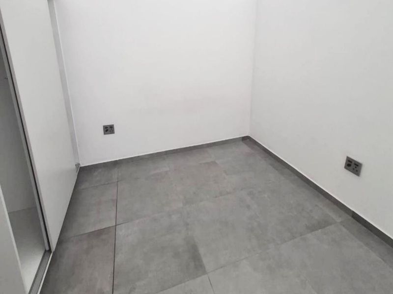 A clean, empty bedroom featuring neutral grey floor tiles, white walls, and a built-in wardrobe with sliding doors.