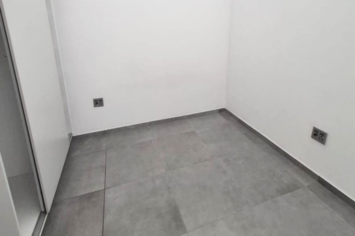 A clean, empty bedroom featuring neutral grey floor tiles, white walls, and a built-in wardrobe with sliding doors.