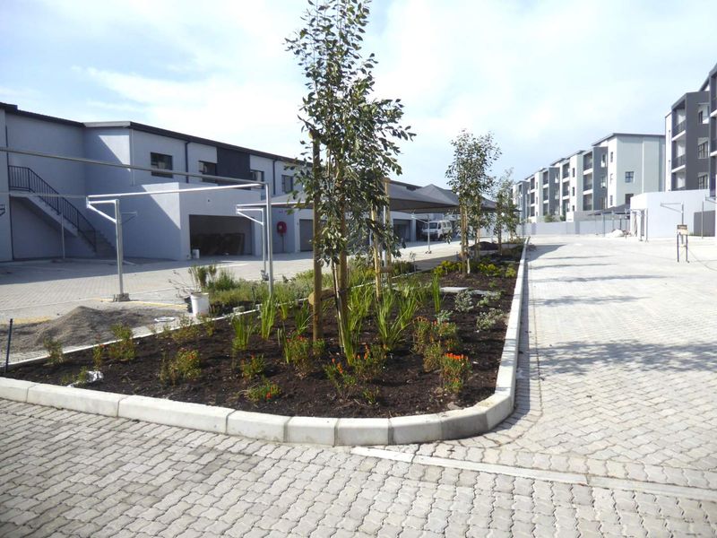 A well-maintained apartment complex exterior featuring paved parking areas, covered carports, and landscaped garden beds.