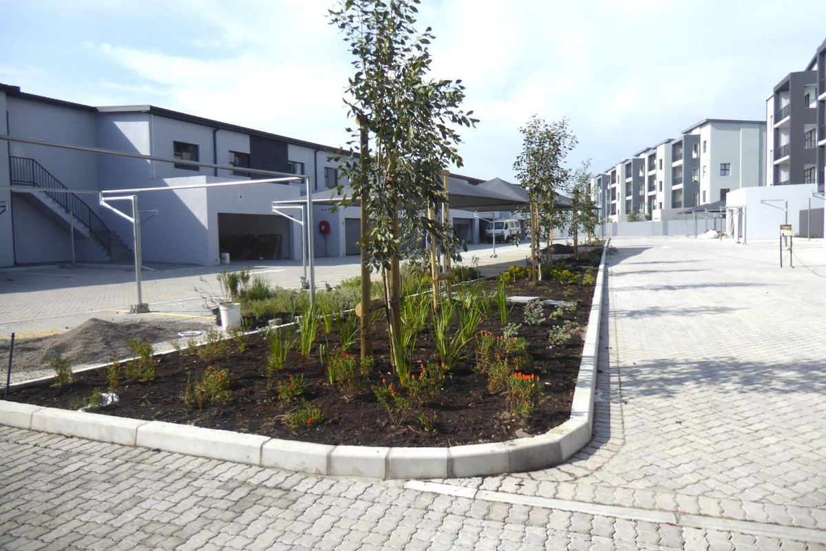 A well-maintained apartment complex exterior featuring paved parking areas, covered carports, and landscaped garden beds.