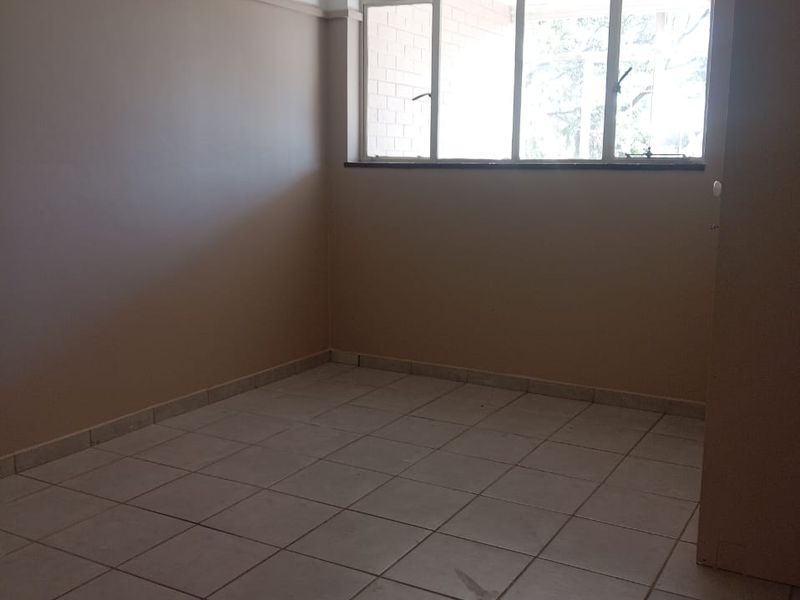 An empty bedroom featuring neutral wall paint, tiled flooring, and a large multi-pane window providing natural light.