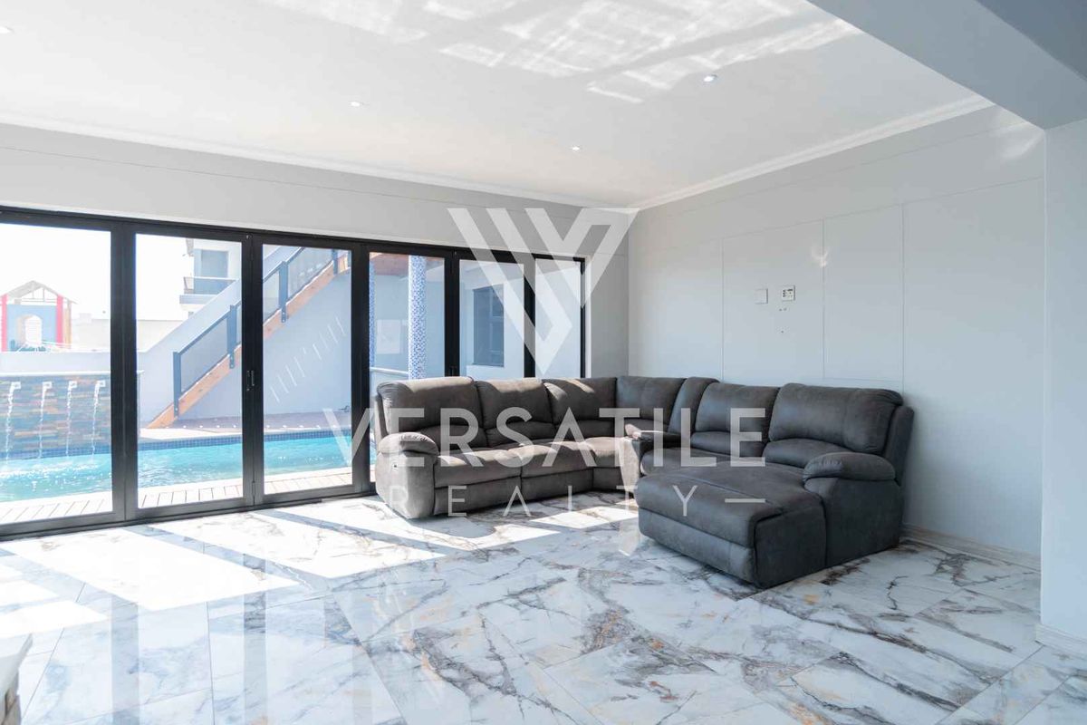 Spacious living area featuring polished marble-look floor tiles, recessed lighting, and large aluminium stacker doors providing seamless access to the pool area.