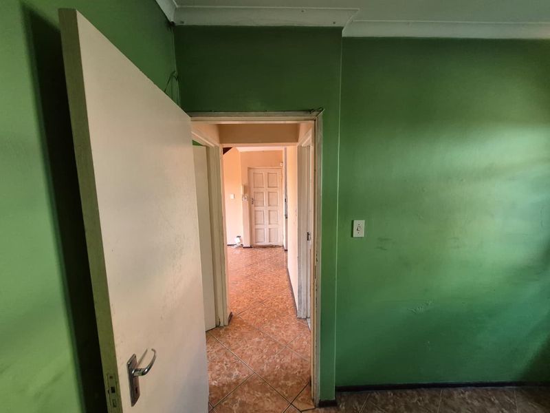 A view through a hallway featuring tiled flooring and green painted walls, leading towards an adjacent room with a panelled door.