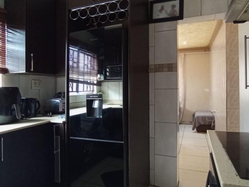 A functional kitchen featuring dark built-in cabinetry, laminate countertops, and ceramic tiling, with an adjacent room visible through the doorway.