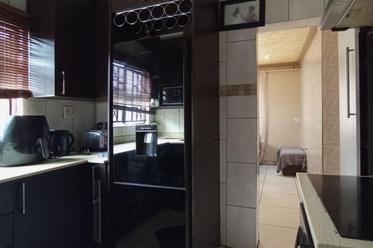 A functional kitchen featuring dark built-in cabinetry, laminate countertops, and ceramic tiling, with an adjacent room visible through the doorway.