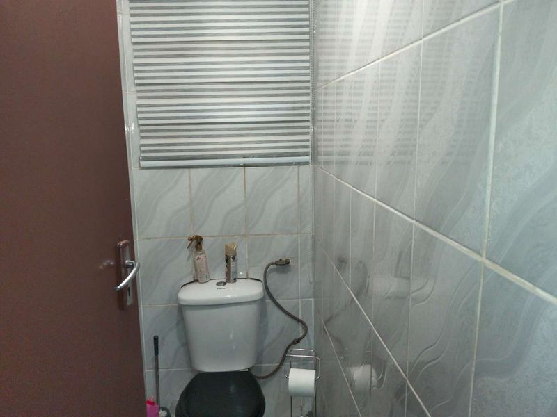 A compact bathroom featuring tiled walls, a standard toilet, and a fitted window blind.