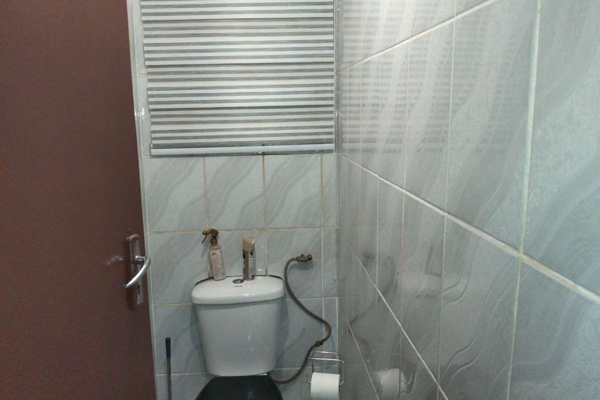 A compact bathroom featuring tiled walls, a standard toilet, and a fitted window blind.