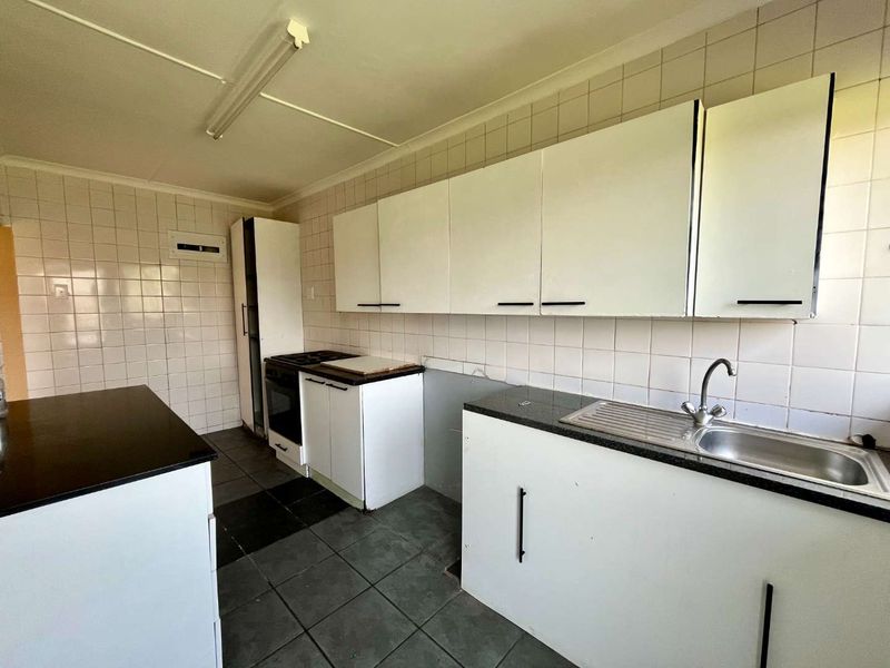 A functional kitchen featuring white cabinetry, tiled splashbacks, dark countertops, and a stainless steel sink, currently in need of cosmetic updates.