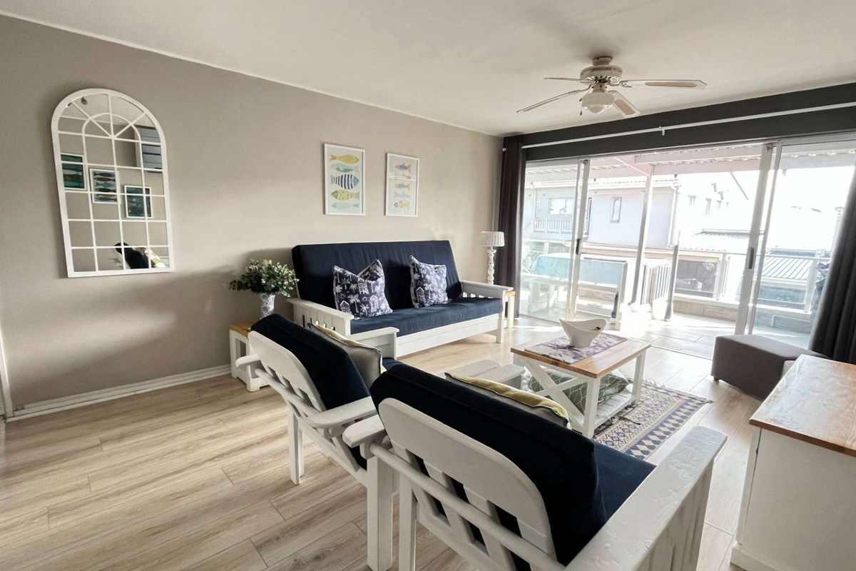 A bright living room featuring laminate flooring, a ceiling fan, and large sliding glass doors that open onto an outdoor balcony area.