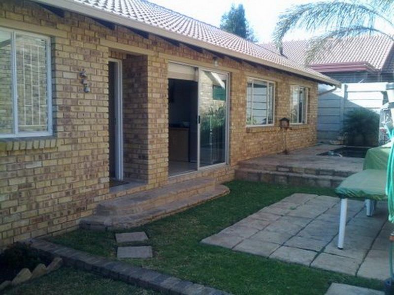 Rear view of a face brick townhouse featuring a paved patio area, sliding glass doors, and a small garden space.