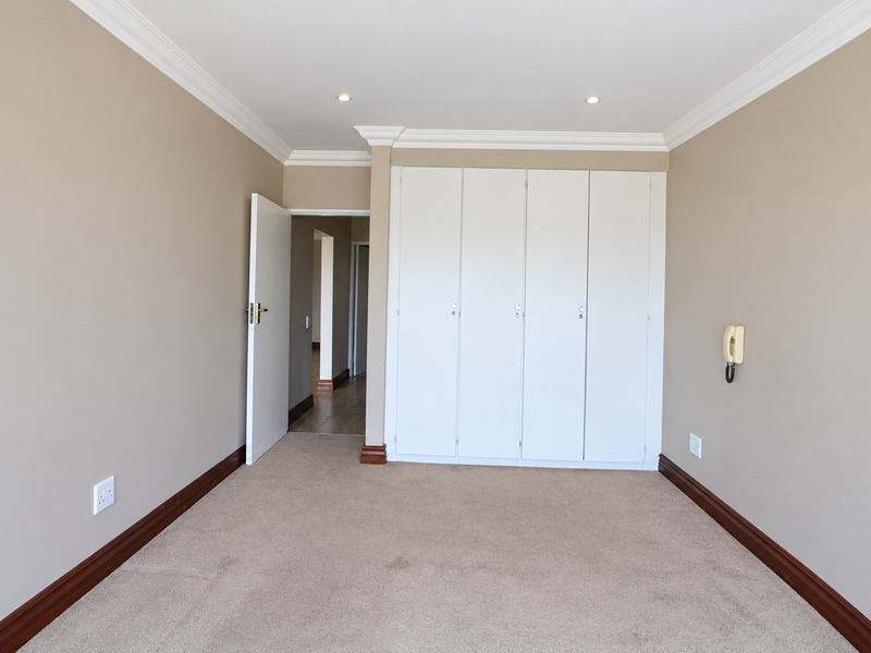 A clean, empty bedroom featuring neutral walls, carpeted flooring, built-in cupboards, and classic cornice detailing.