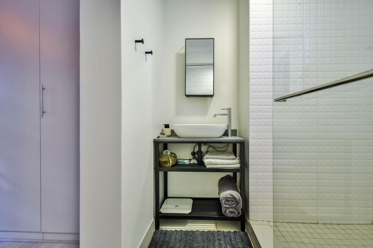 A modern bathroom featuring a vessel sink vanity, wall-mounted mirror, and a glass-enclosed shower with white tiled walls.