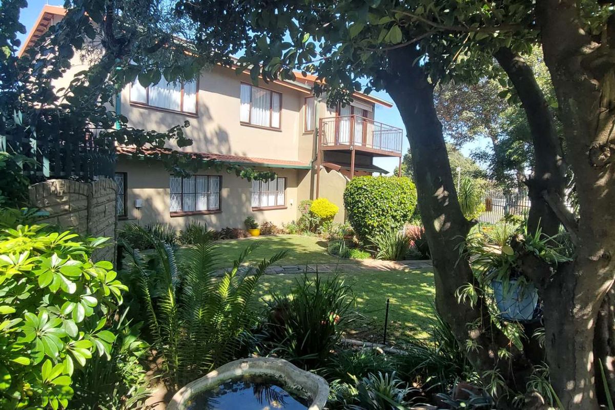 Rear view of a two-story residential house featuring a balcony, established garden, and paved pathways.